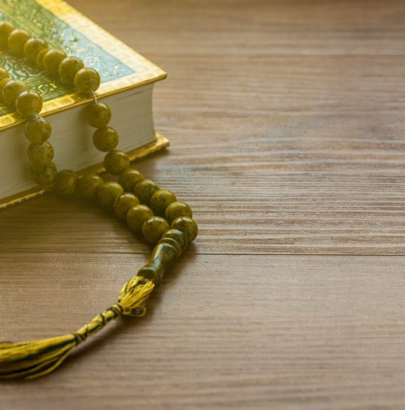 Selective focus of rosary beads and Quran on a wooden background with copy space.