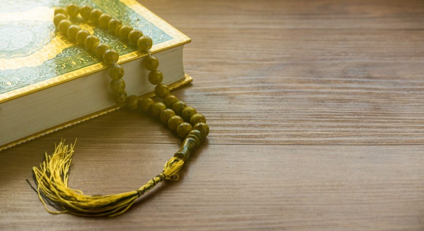 Selective focus of rosary beads and Quran on a wooden background with copy space.